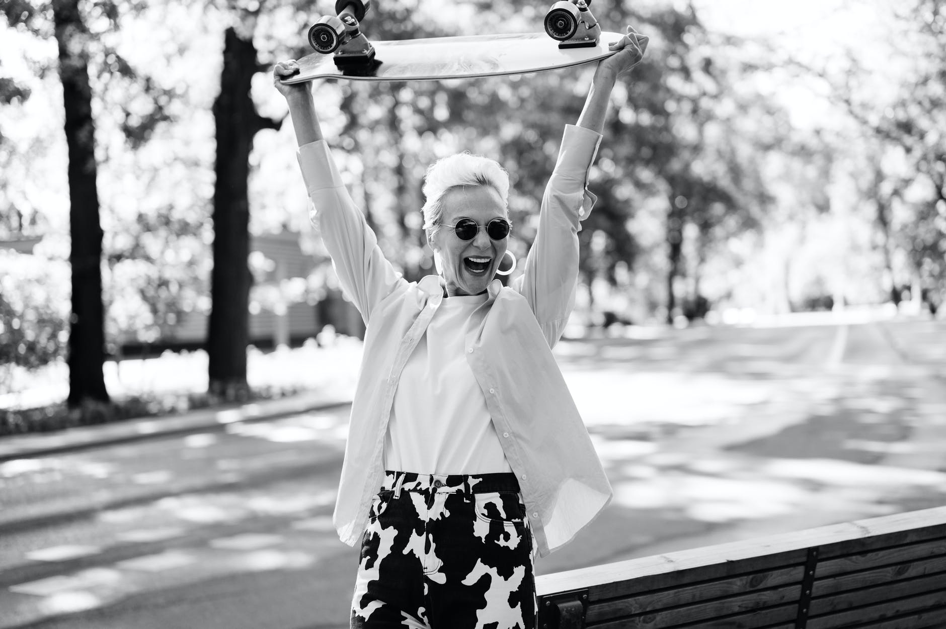 grayscale photo of a woman holding a skateboard above her head
